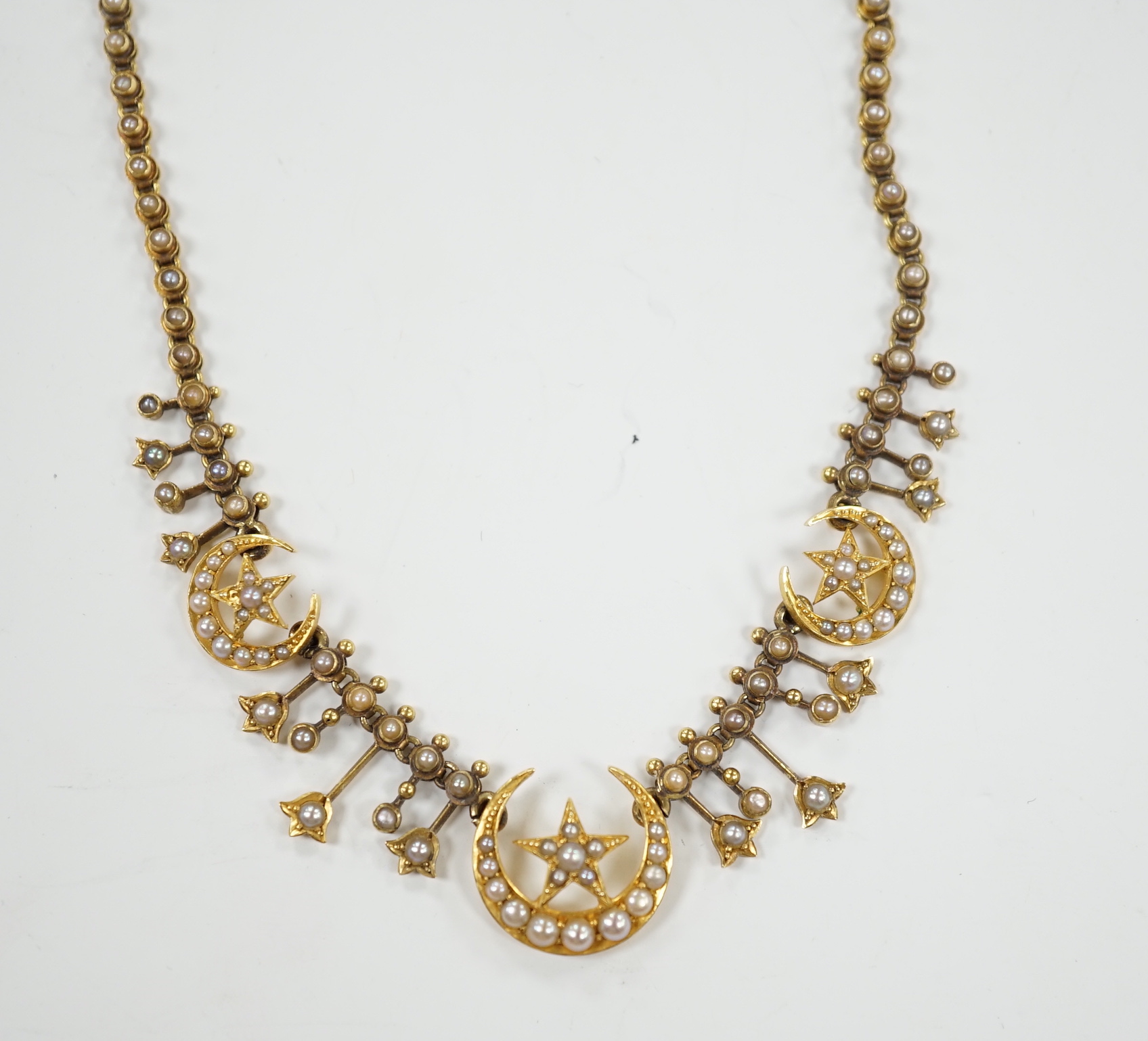 An Edwardian yellow metal and seed pearl set drop necklace, with star and crescent motifs, lacking central drop, 38cm, gross weight 16.3 grams.